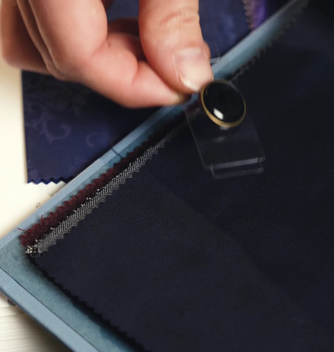 A hand holding a button against navy suiting cloth